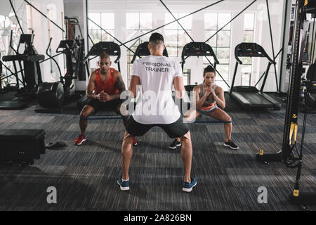 Vista posteriore del personal trainer di supervisione atleti multiculturale il riscaldamento in palestra Foto Stock