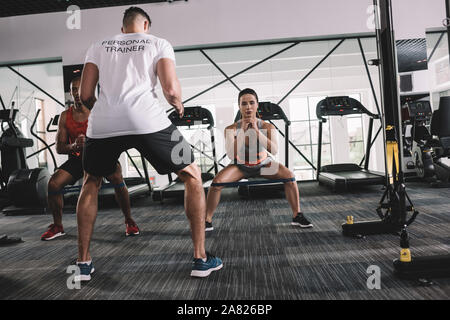 Vista posteriore del personal trainer in piedi vicino atleti multiculturale il riscaldamento in palestra Foto Stock