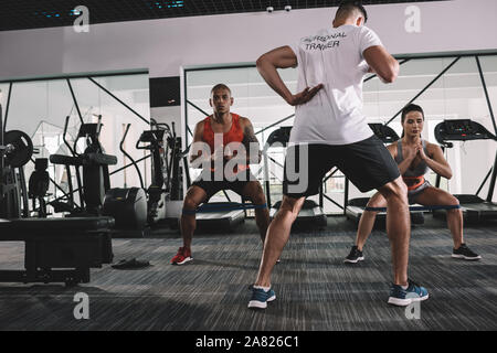 Vista posteriore del personal trainer il riscaldamento in palestra insieme con gli atleti multiculturale Foto Stock