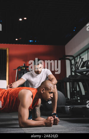 Attento trainer istruire african american sportivo facendo esercizio tavoloni Foto Stock