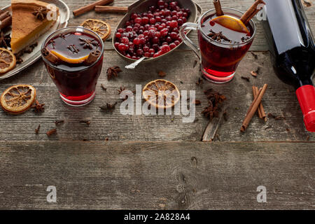 Speziato rosso vino brulé vicino a bottiglia e un pezzo di torta, bacche, anice, fettine di arancia e cannella su legno tavolo rustico con spazio di copia Foto Stock