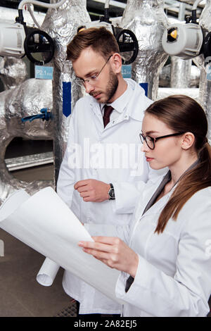 Gli ingegneri in camici guardando blueprint vicino il sistema del compressore d'aria Foto Stock