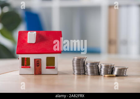 Modello di casa nei pressi di pile di oro e di argento monete sul tavolo di legno Foto Stock