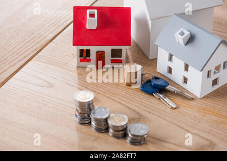 Modelli della casa vicino alle chiavi e pile di oro e di argento monete sul tavolo di legno Foto Stock