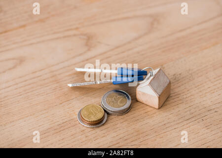 I tasti con toy house gingillo vicino a golden e silver monete sul tavolo di legno Foto Stock