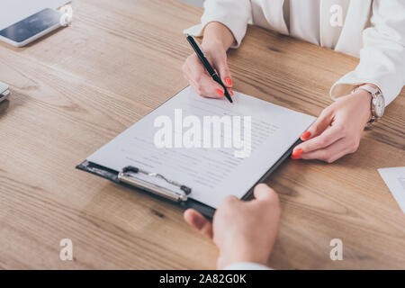 Vista parziale di imprenditore tenendo negli appunti e donna firma contratto Foto Stock