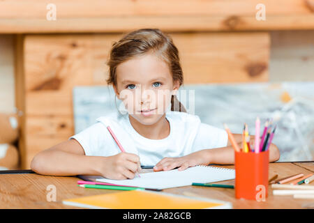 Messa a fuoco selettiva di carino bambino guardando la fotocamera durante il disegno su carta alla scuola d'arte Foto Stock