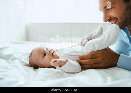 Padre Felice toccando carino piccola figlia giacente sulla biancheria da letto bianca Foto Stock