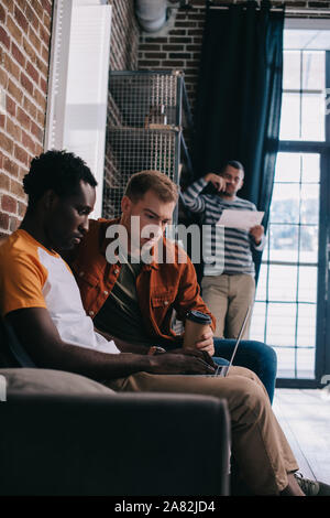 Considerato americano africano uomo d affari con computer portatile mentre è seduto sul divano vicino a un collega Foto Stock