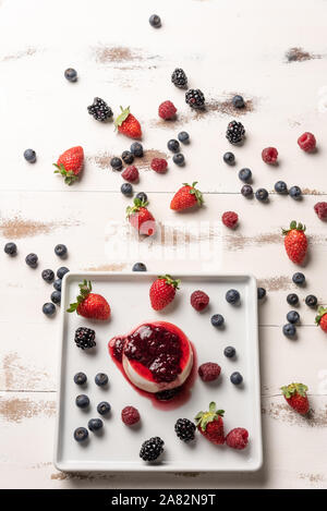 Deliziosi dessert italiano panna cotta con salsa di bacche e frutti di bosco freschi in bianco sullo sfondo di legno Foto Stock