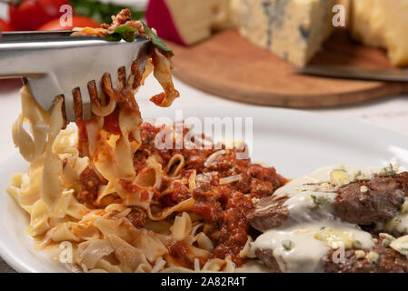 Pappardelle fatte in casa la pasta con la salsa di pomodoro e carne bovina mignon con salsa al formaggio in una piastra bianca di legno su sfondo bianco, morbido e leggero Foto Stock