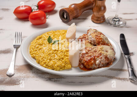 Risotto allo Zafferano con la parmigiana bistecca di manzo. Risoto e carni bovine in una piastra bianca di legno su sfondo bianco. Luce morbida. Il cibo italiano. Risotto con curcum Foto Stock