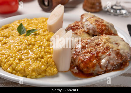 Risotto allo Zafferano con la parmigiana bistecca di manzo. Risoto e carni bovine in una piastra bianca di legno su sfondo bianco. Luce morbida. Il cibo italiano. Risotto con curcum Foto Stock