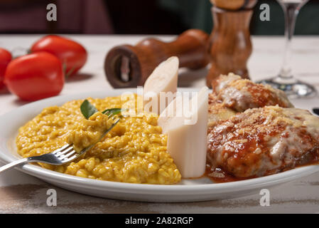 Risotto allo Zafferano con la parmigiana bistecca di manzo. Risoto e carni bovine in una piastra bianca di legno su sfondo bianco. Luce morbida. Il cibo italiano. Risotto con curcum Foto Stock