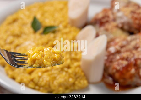 Risotto allo Zafferano con la parmigiana bistecca di manzo. Risoto e carni bovine in una piastra bianca di legno su sfondo bianco. Luce morbida. Il cibo italiano. Risotto con curcum Foto Stock