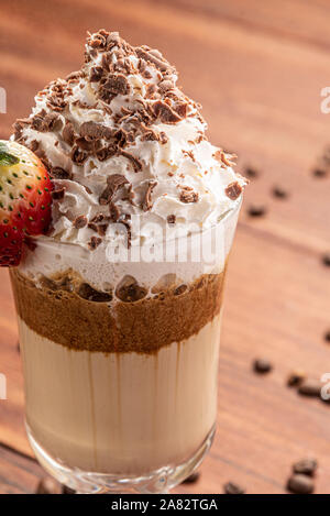 Il freddo bevanda caffè frappé (frappuccino), con panna e cioccolato di naselli, con grani di caffè su sfondo di legno Foto Stock