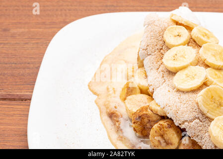 Tapioca riempito con banana e cannella e latte condensato, su sfondo di legno. Flatbread realizzato da manioca (noto anche come casabe, ingaggiami, beiju, bob, b Foto Stock