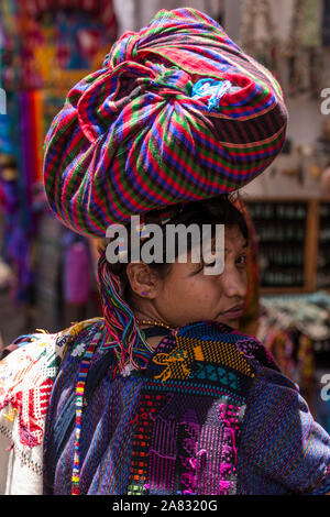 Giovane donna di Sang Antonio Palopo al mercato a Chichicastenango, Guatemala portando la sua merce sul suo capo, guardando indietro sopra la sua spalla. Ella Foto Stock