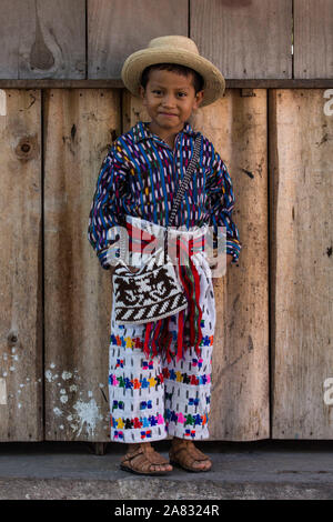 Giovane ragazzo Maya, età 6, indossando vestiti tradizionali di San Pedro La Laguna, Guatemala, comporta per un ritratto di fronte a un muro non verniciata. Foto Stock