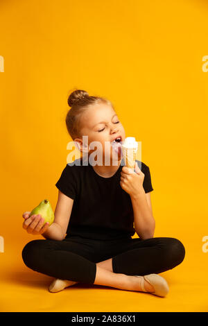 Carino little ballerina scegliendo tra apple e il dolce di gelati su sfondo giallo Foto Stock