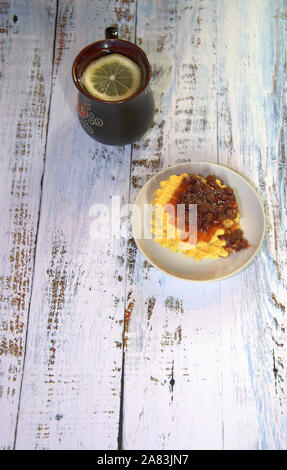 Una ceramica nera tazza di tè con una fettina di limone e una piastra con cialde Viennese e confettura di fragole. Close-up. Foto Stock
