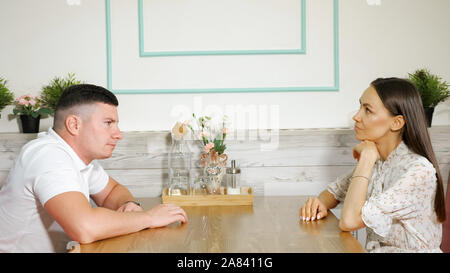 Giovane uomo preoccupato tocchi le dita sul tavolo di legno seduto di fronte a gravi bella donna in luce accogliente caffetteria Foto Stock