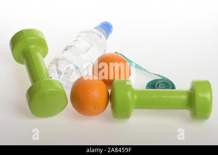 Manubri in colore verde brillante, acqua in bottiglia, misurare il nastro e frutta su sfondo grigio chiaro. Barbells vicino succosa di colore arancione. Sport e regime sano attrezzatura. Atletica leggera perdita del peso e di concetto Foto Stock