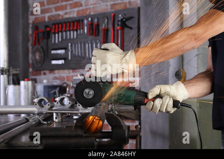 Man mano il lavoro in officina di casa garage taglio tubo di metallo, con costruzione di guanti, taglio di metallo fa scintille closeup, fai da te e del concetto di artigianato Foto Stock