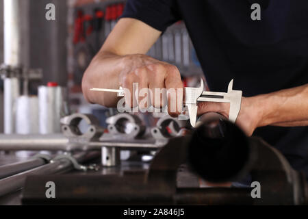 Mani uomo closeup lavoro in officina di casa garage con misura della pinza della tubazione metallica fissata ad una morsa sul banco di lavoro, fai da te e del concetto di artigianato Foto Stock