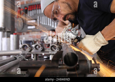 Uomo lavoro in officina di casa garage con smerigliatrice angolare, occhiali di protezione e guanti di costruzione, metallo levigatura fa scintille closeup, fai da te e del concetto di artigianato Foto Stock