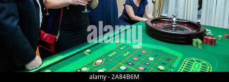 Gruppo di persone dietro alla roulette tavolo da gioco nel casino di lusso. Gli amici a giocare a poker al tavolo della roulette con nastro di misurazione. Vegas giochi vita notturna fortunato concetto vincente. Banner Foto Stock