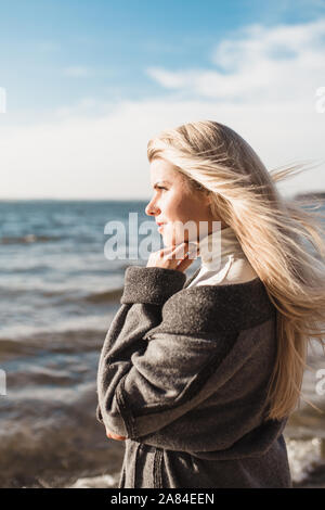 Felice slim affascinante bionda con grandi occhi blu e un sorriso gode di felicità in riva al mare Foto Stock