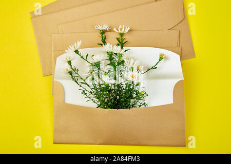 Busta in oro con una molla floreale su sfondo giallo. Appartamento laico, vista dall'alto. Aperta la busta. Messaggio di saluto festivo concept Foto Stock