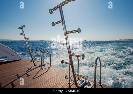 Metallo Acciaio scale sul retro pontatura in teak di un lussuoso yacht a motore vela su un oceano tropicale con sfondo con cielo nuvoloso Foto Stock