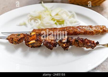 Uyghur Tradizionale Calda succulento agnello speziata e spiedini di carne di manzo con cumino e cipolle su una piastra bianca Foto Stock
