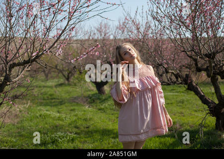 Felice donna bionda in abito rosa passeggiate attraverso il giardino fiorito in primavera Foto Stock