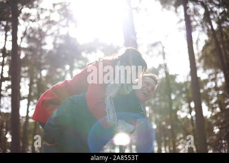 Felice, giocoso giovane piggybacking nella soleggiata, Boschi di autunno Foto Stock
