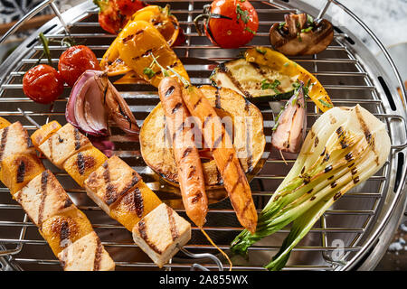 Ortaggi freschi la cottura alla griglia su un barbecue in inverno con le carote, butternut, finocchio, pepe dolce, pomodoro e halloumi o tofu spiedini Foto Stock