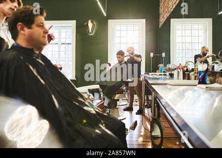 I clienti maschi e barbieri in Barberia Foto Stock