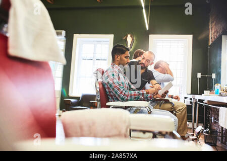 Barbiere maschio e il cliente con la tavoletta digitale parlando in Barberia Foto Stock