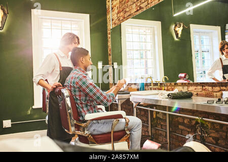 Barbiere maschio e il cliente con la tavoletta digitale parlando in Barberia Foto Stock