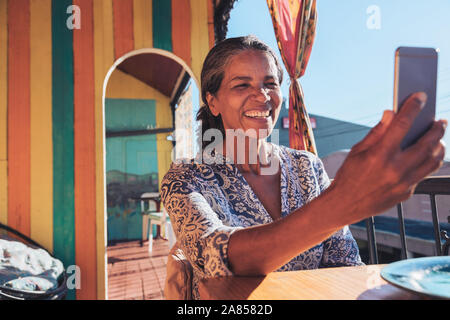 Sorridente, donna felice tenendo selfie con smart phone sul patio soleggiato Foto Stock