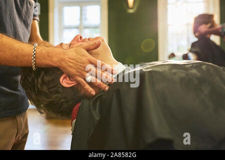 Barbiere maschio massaggiare viso della cliente in Barberia Foto Stock