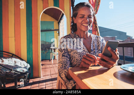 Sorridente, donna felice utilizzando smart phone sul soleggiato balcone ristorante Foto Stock