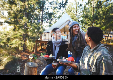 Happy amici a ridere e mangiare al campeggio nel bosco Foto Stock