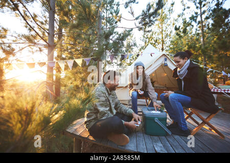 Gli amici a giocare a carte al di fuori yurta al sunny campeggio nel bosco Foto Stock