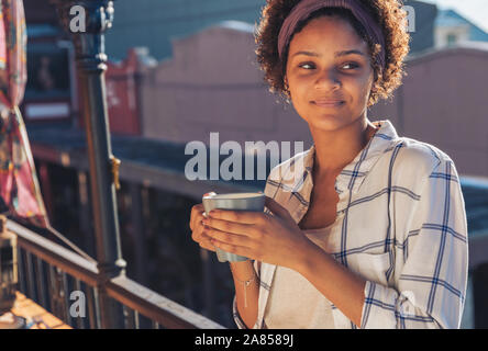 Sorridente giovane donna di bere il caffè sul balcone soleggiato Foto Stock
