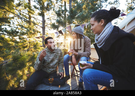 Gli amici a bere vino e a parlare a sunny campeggio nel bosco Foto Stock