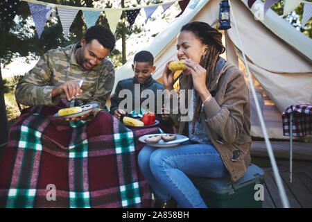 Famiglia mangiare sulla pannocchia di mais al campeggio Foto Stock