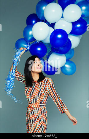 Sorridente e spensierato donna con blu e bianco grappolo a palloncino Foto Stock